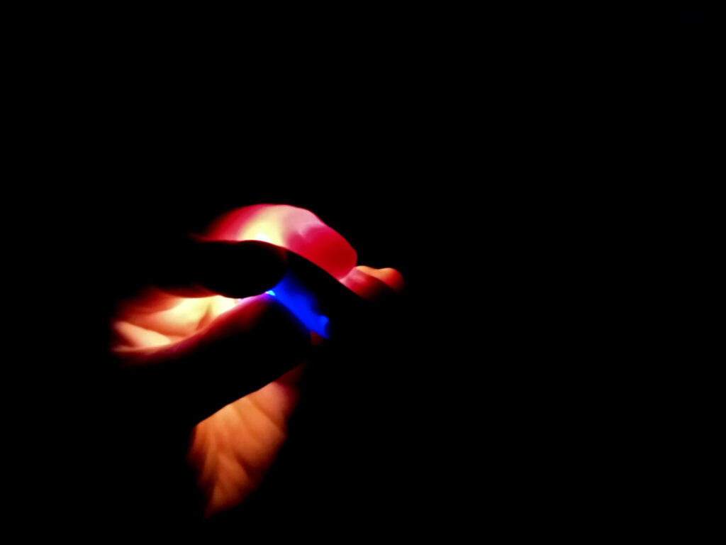 glowing red fingers hold a blue lozenge-shaped device in a totally black room