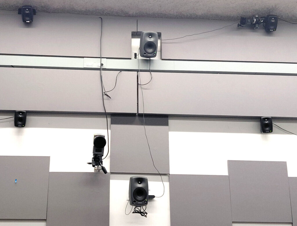 small loudspeakers arranged in diamond formation against a wall of white and gray panels